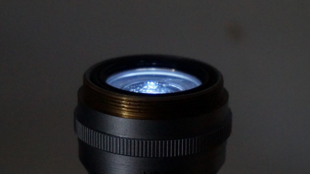 D.I.Y. collector lens being illuminated with an led flashlight from above and being viewed from an oblique angle. The lower edge of the top lens in the pack is still visible and the illumination beam clearly visible. There is a much greater angle that this condenser will be able to see than the 1.4 achromat. Image is deliberately upside down.