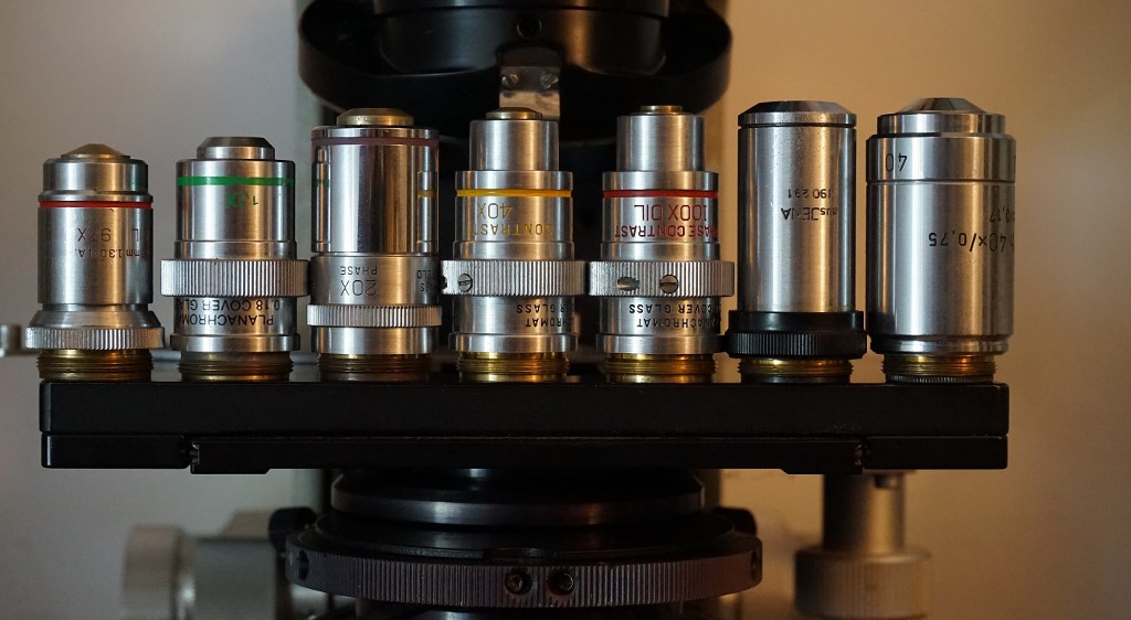 A set of phase contrast objectives; 10X .25, 20X .50 , 40X .65 and 100X 1.25 planachromats flanked by a conventional 97X 1.30 B &amp; L 160mm objective on the left and a couple of D.I.N. objectives on the right.